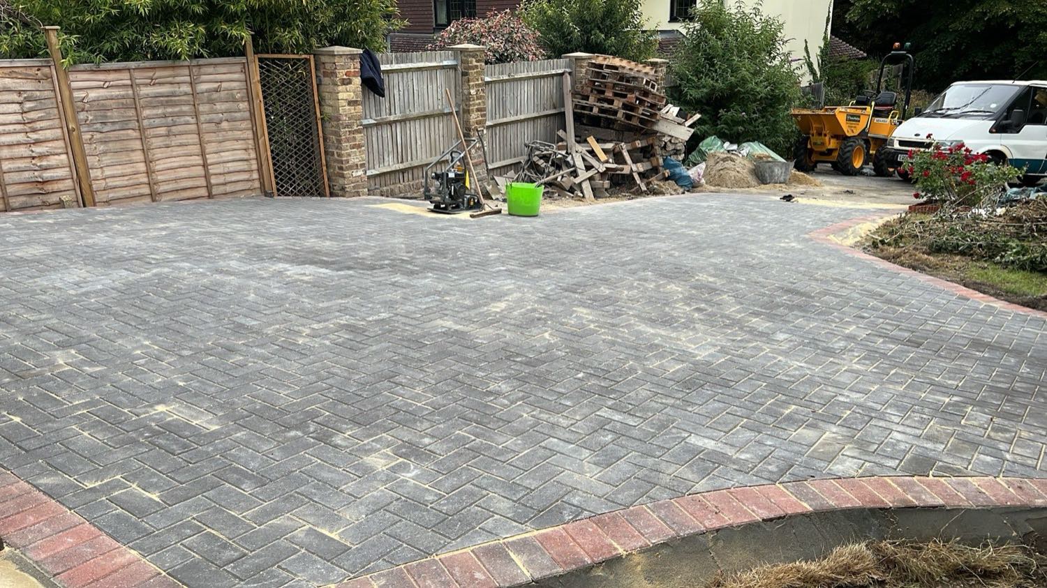 Charcoal block paving going down over a consolidated base, edged with a brick soldier course. The dumper is still on site — this is the stage most contractors never photograph.